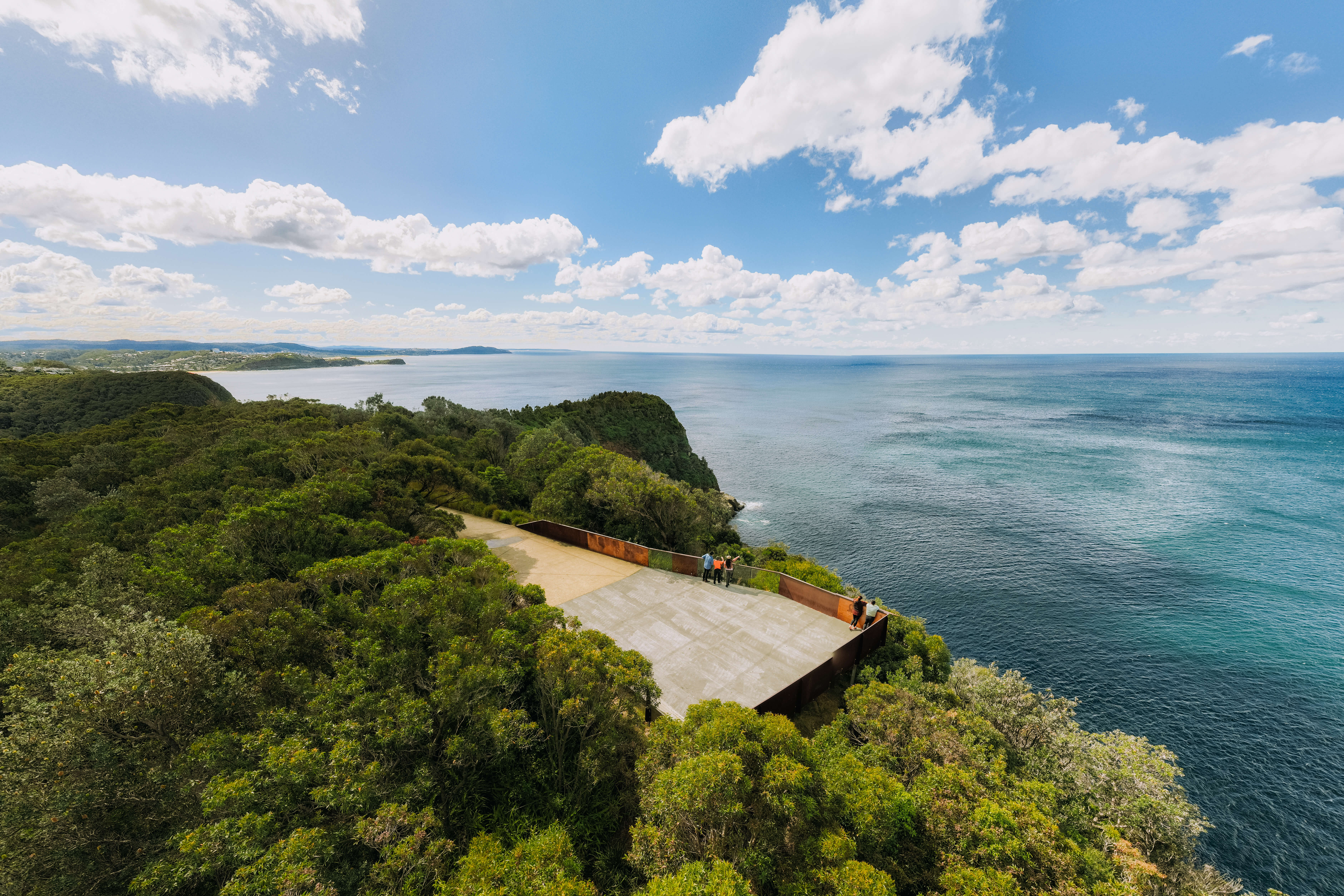 Photo of a look out platform surrounded by lush green bushland overlooking the blue-green open ocean.