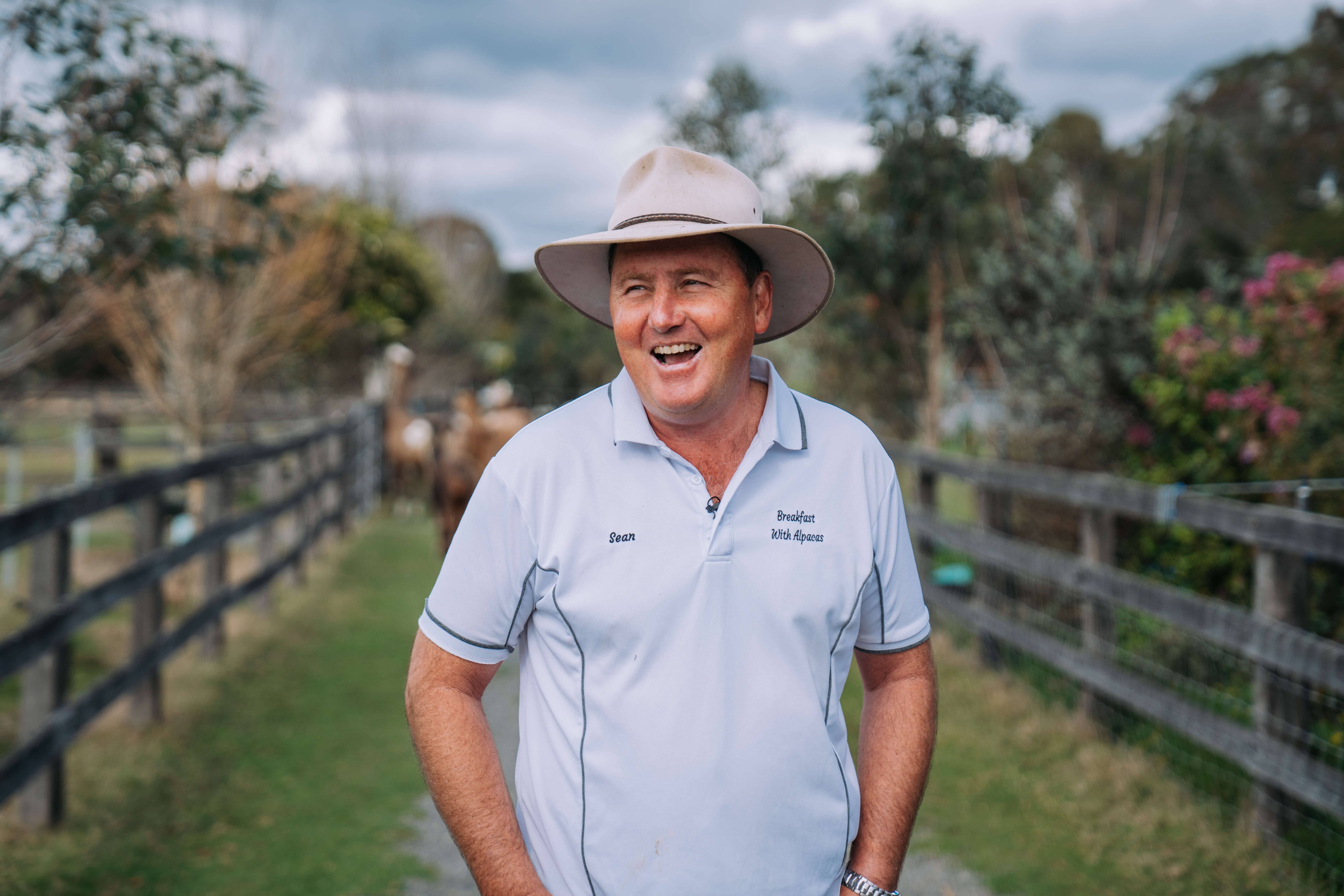 A man wearing a wide brimmed hat and light blue shirt smiling off in the distance
