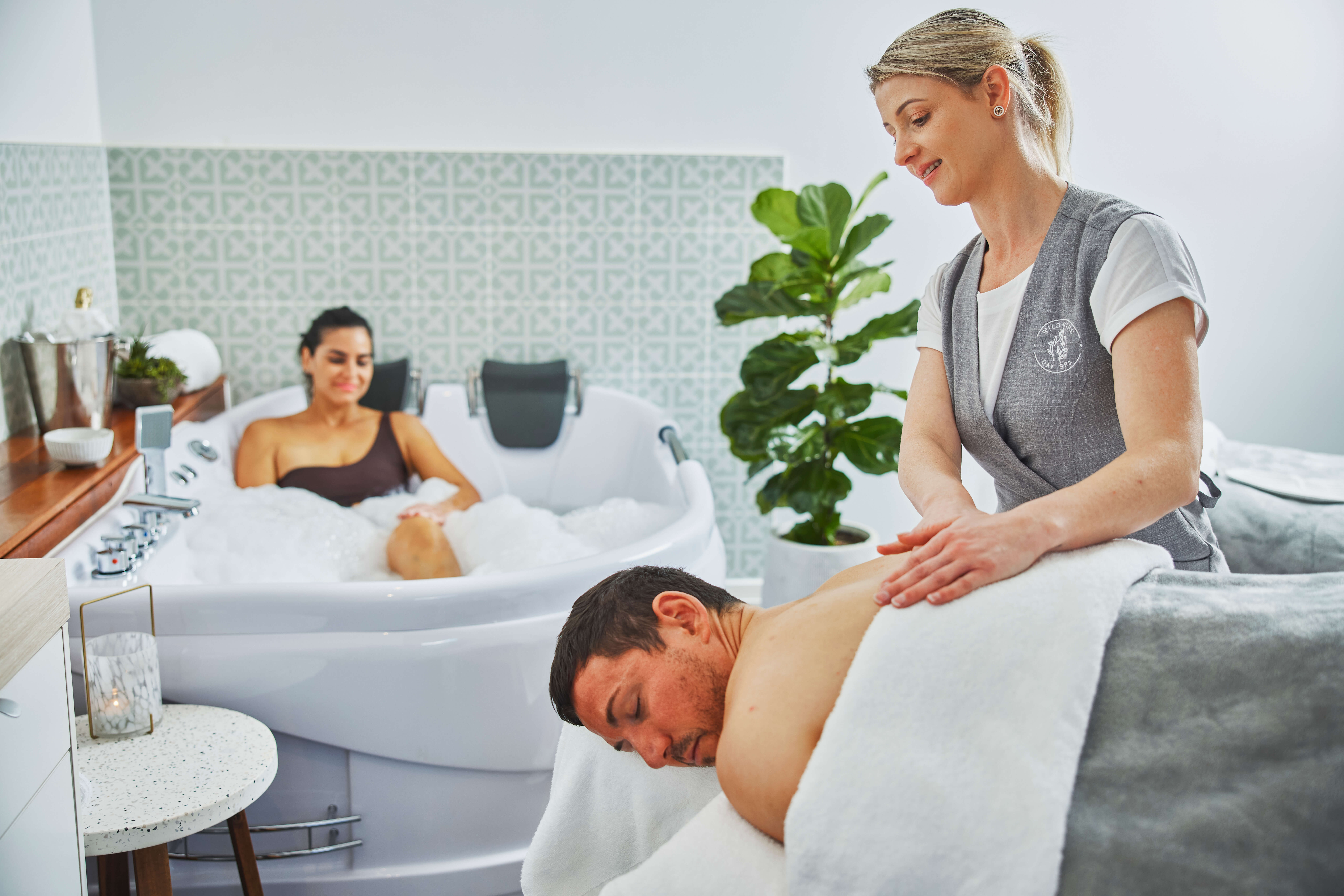 A lady sitting in a spa tub, and a man laying on a massage table receiving a back massage