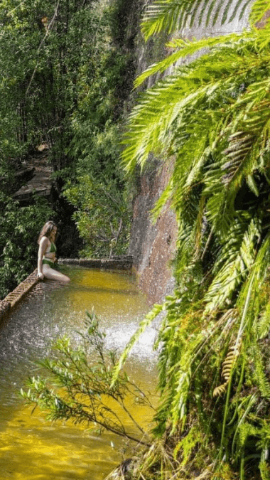 Woman sits on waters edge in bikini.