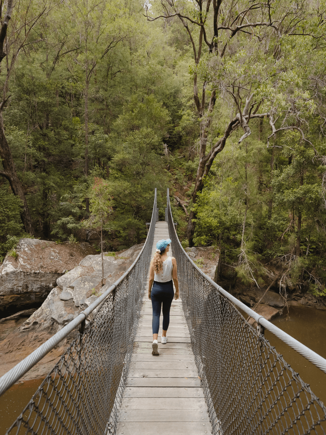 A lady in fitness gear walking across a suspension bridge in a rainforest.